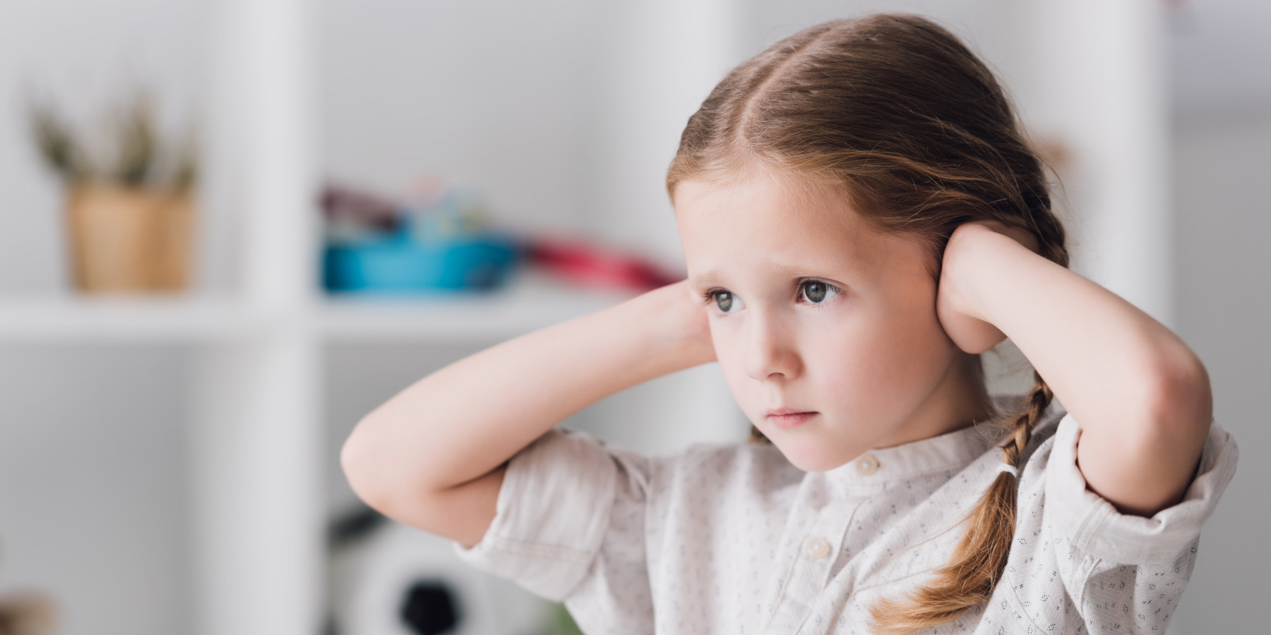 Nahaufnahme eines kleinen Kindes, das die Ohren mit den Händen bedeckt und wegschaut